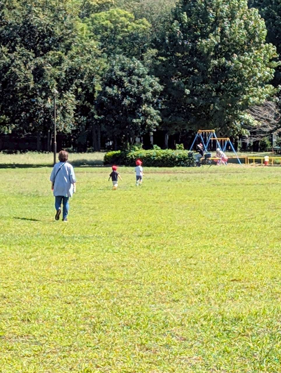 広い芝生の公園で先生と一緒に走る園児たち